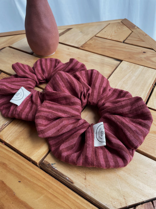 Two maroon scrunchies on a wooden surface with a blurred background