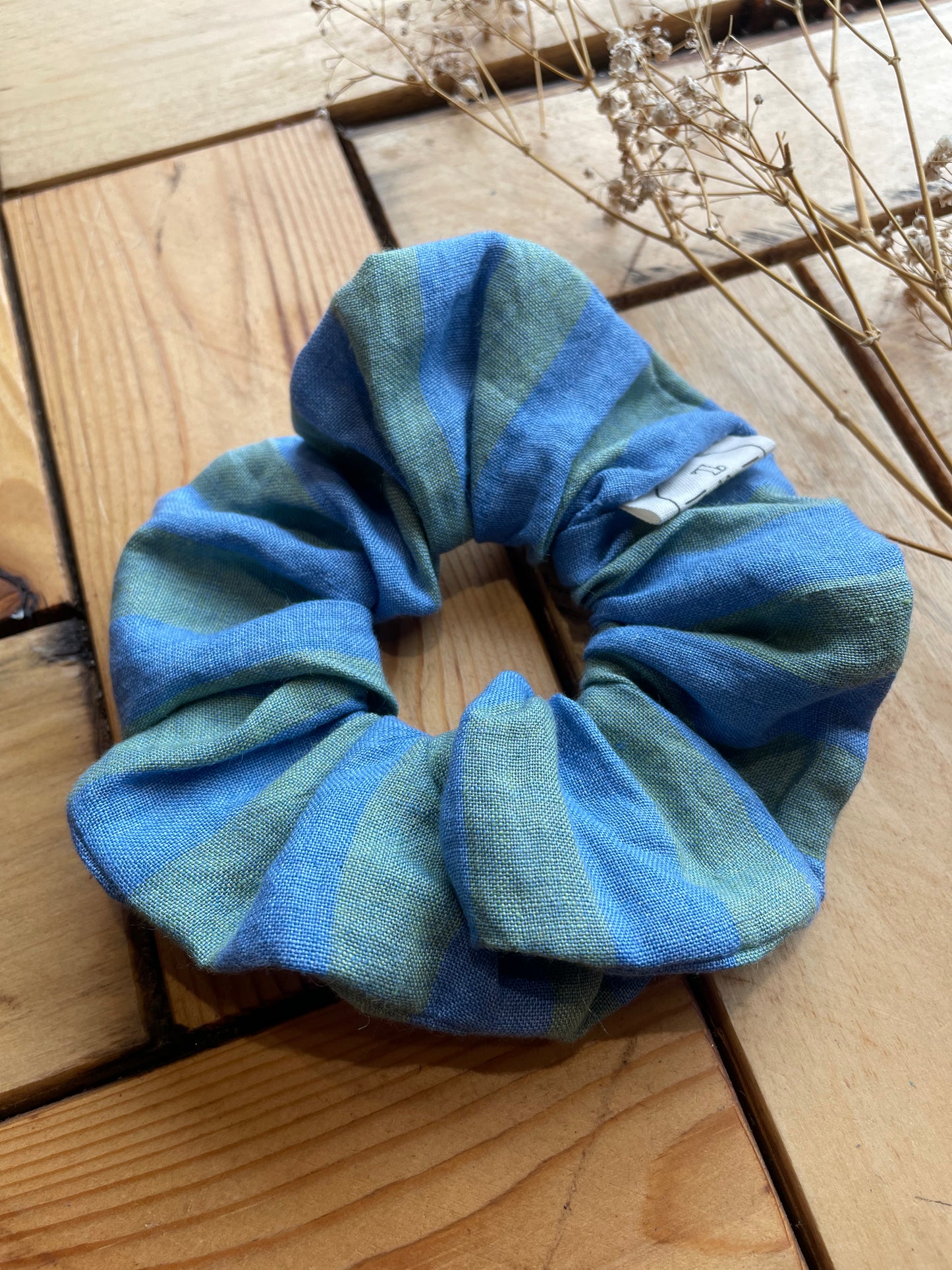 Blue and green striped scrunchie on a wooden surface with dried plants
