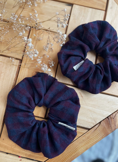 Two purple check linen scrunchies on a wooden surface with dried flowers.