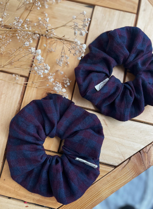 Two purple check linen scrunchies on a wooden surface with dried flowers.