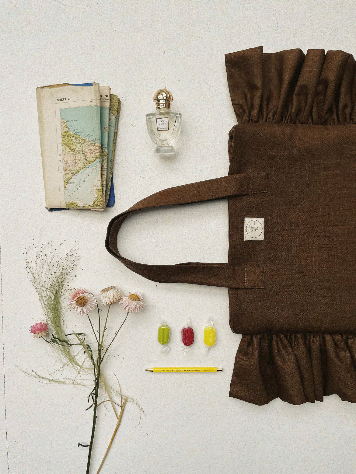 Flat lay with Irish linen brown ruffle bag, sweets, a map, perfume and dried flowers