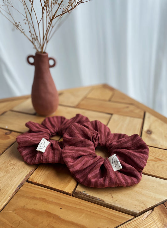 Two striped scrunchies with labels on a wooden table with a vase in the background.