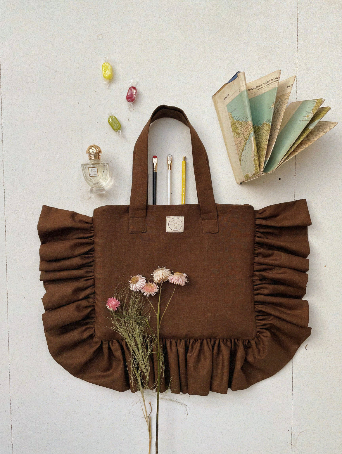 A brown ruffle tote bag made from Irish linen, displayed with a map, a book, and decorative items.