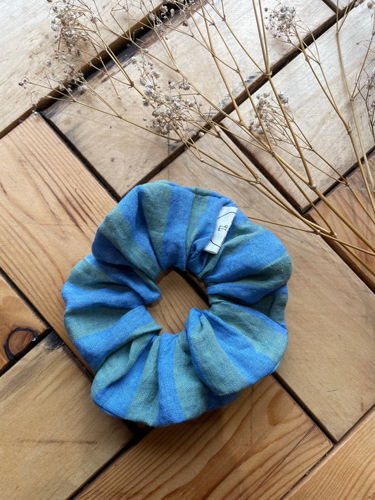 Blue and green striped scrunchie on a wooden surface with dried plants