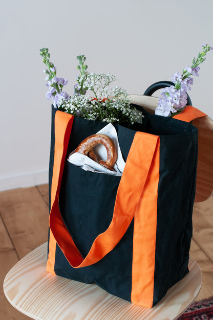 A black and orange tote bag with two large exterior pockets and multiple interior pockets, adorned with a floral arrangement.