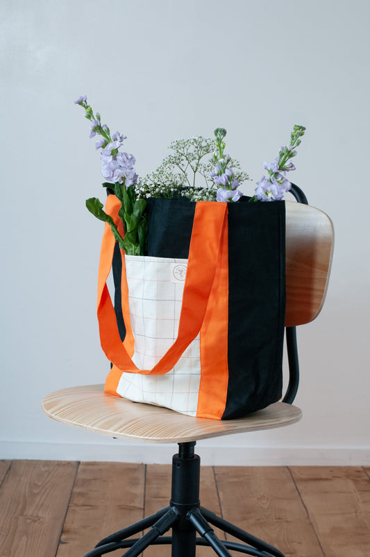 A black and orange tote bag with two large exterior pockets and multiple interior pockets, adorned with a floral arrangement.