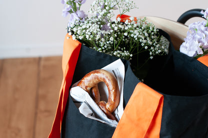 A black and orange tote bag with two large exterior pockets and multiple interior pockets, adorned with a floral arrangement.