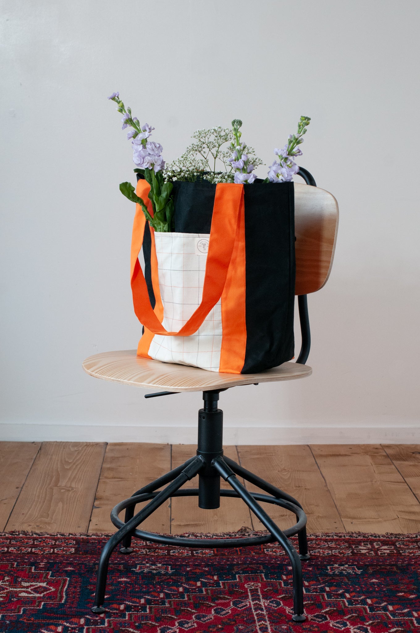 A black and orange tote bag with two large exterior pockets and multiple interior pockets, adorned with a floral arrangement.