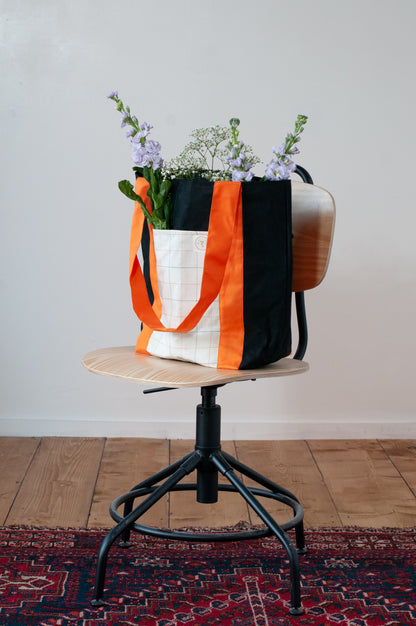 A black and orange tote bag with two large exterior pockets and multiple interior pockets, adorned with a floral arrangement.