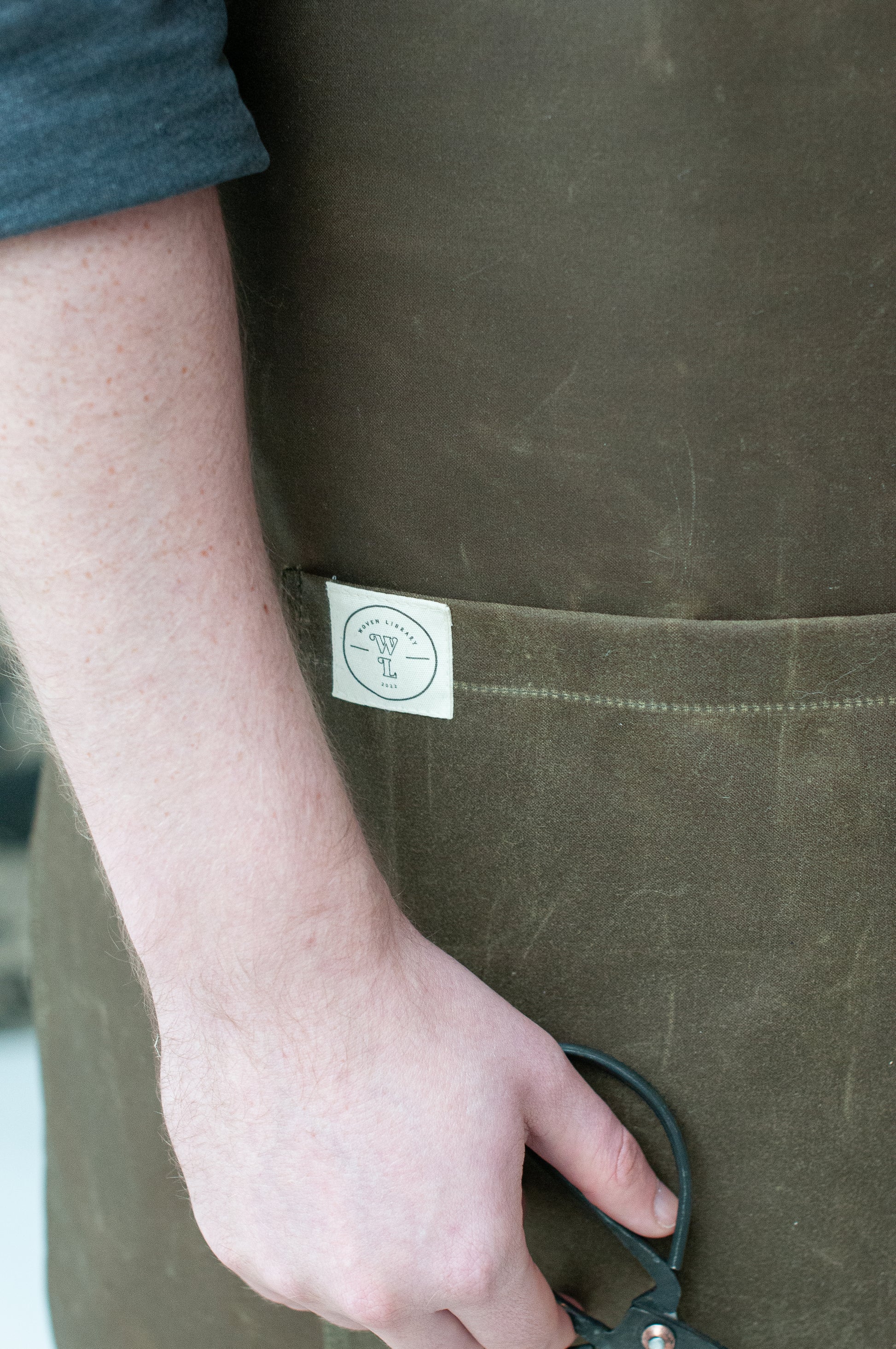 close up of a pocket on a wax cotton apron on a khaki brown worn by a person
